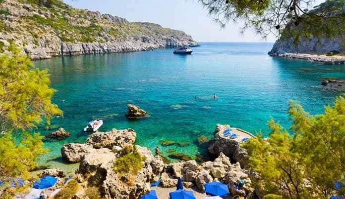 The turquoise cove of Anthony Quinn Bay and its pine-clad cliffs